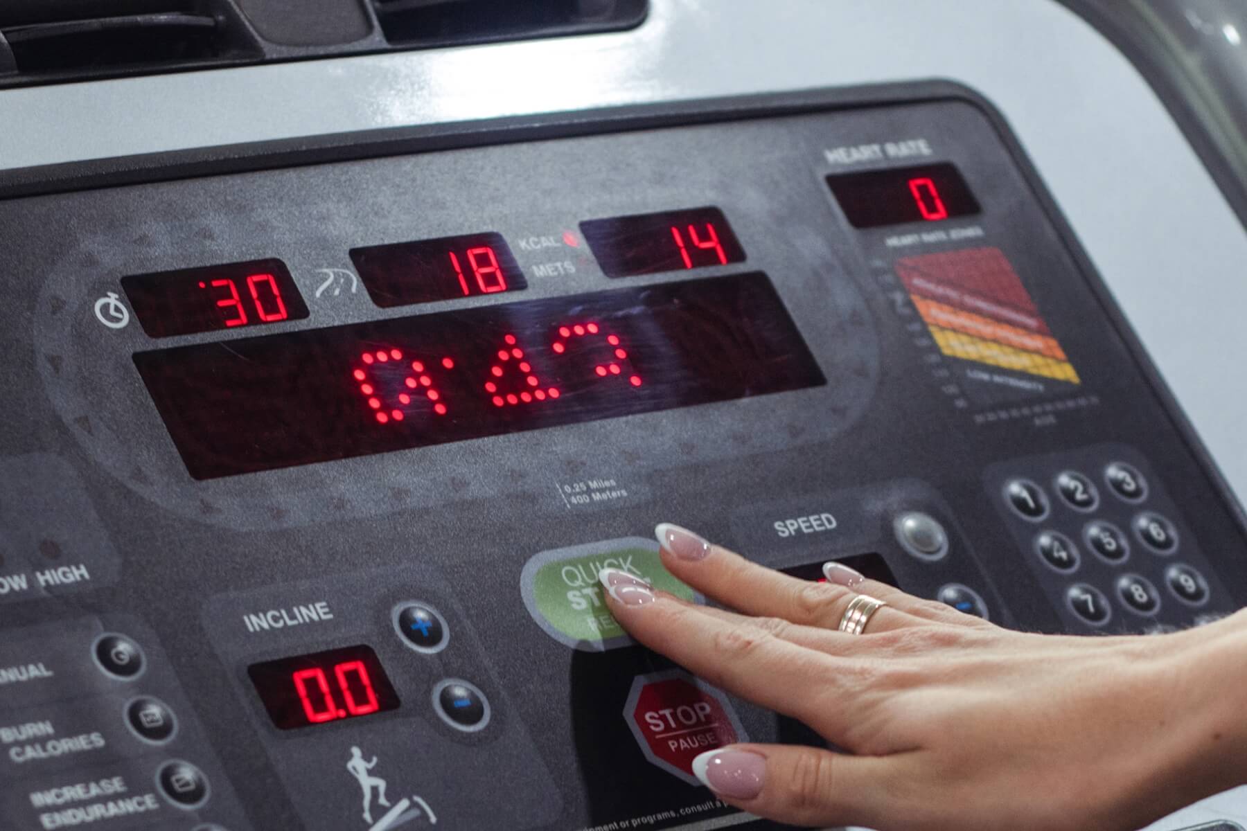 Young woman's hand pressing start button on treadmill during cardio workout session